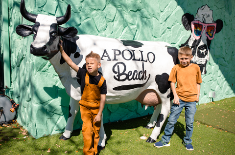 Two children standing next to a cow sculpture with 'Apollo Beach' branding.